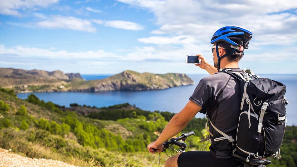 un jeune homme sur une piste de VTT en Espagne et prend une photo sur un téléphone blanc en arrière-plan de la mer Méditerranée de la Costa Brava. route de montagne près de la ville de Cadaques